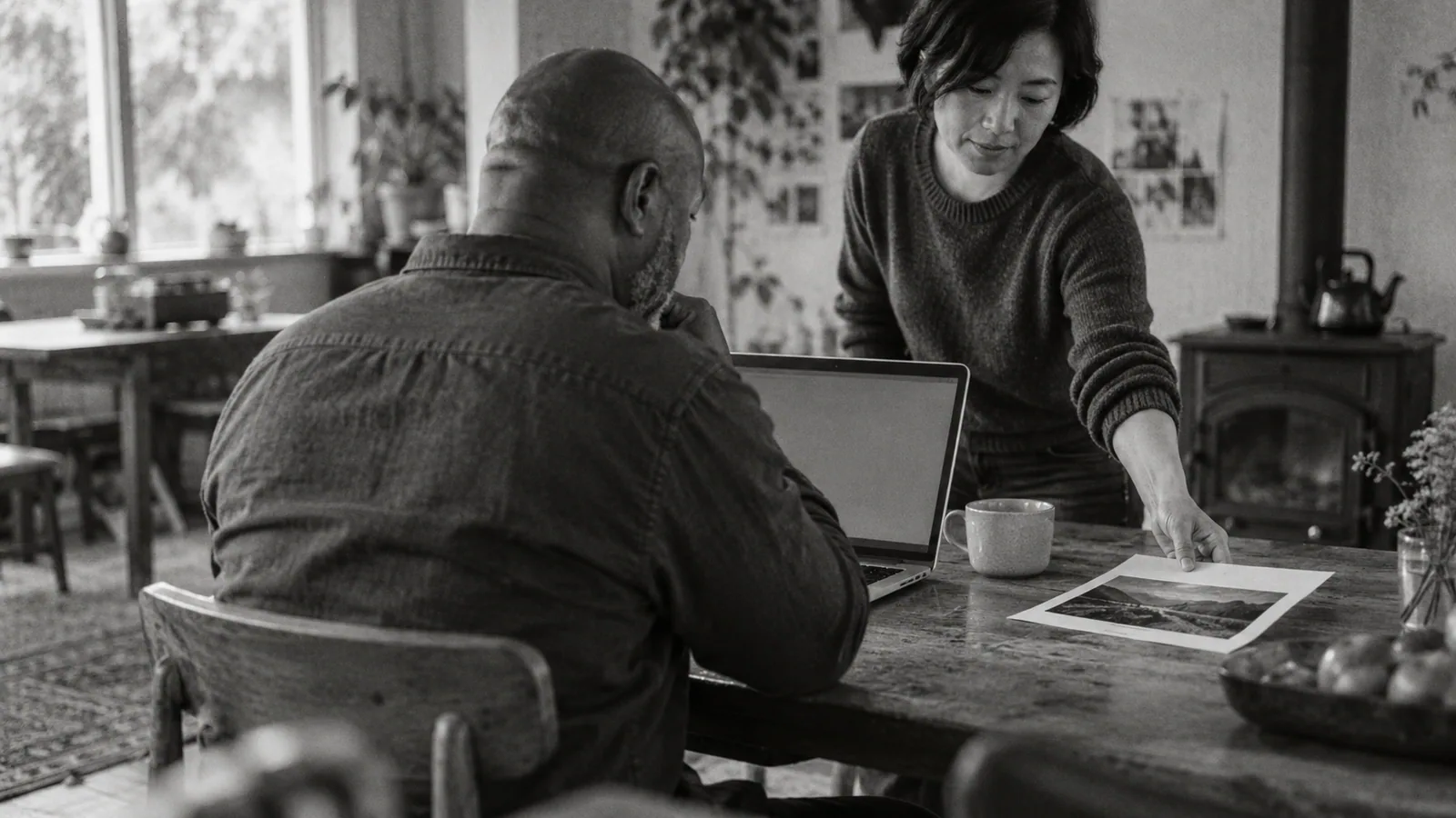 Generated black-and-white editorial photograph: A buyer checks a laptop beside a printed reference.